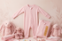 Organic bamboo baby romper in pink, surrounded by soft toys and baby accessories, showcasing comfort and style.